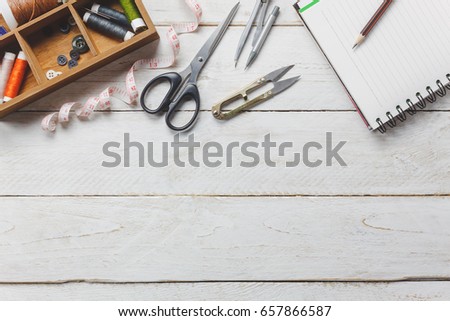 Top view accessories tailor concept.Tailor tools is cutting scissors, spools of thread,tape measurement,buttons and sewing clothes. Notebook for free space text on rustic wooden background.