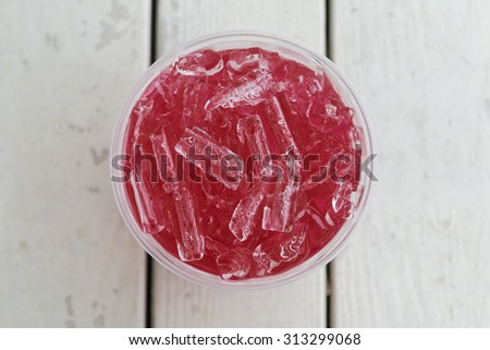 Cold red color drink in clear plastic cup with ice