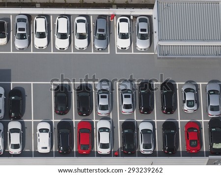 Top view photo of parking lot, taken from 46th floor of skyscraper, with varieties of colored vehicles such as yellow, white, black, grey, silver and blue.