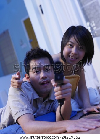 A man holding a game gadget aiming to the camera while the woman watch