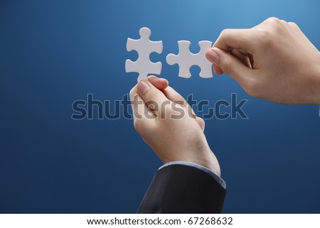 Human hand fitting two puzzle pieces together.