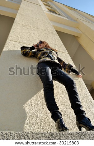 Young woman standing at the wall in sun glasses, turned away from sun, low angle view