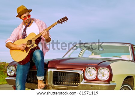 The young guy plays on a guitar sitting on a cowl of the old car