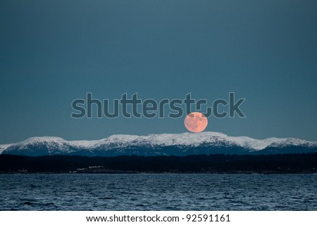 Rise up of beautiful red moon over the snowy Norwegian mountains