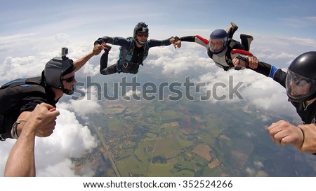 A group of friends holding hands teamwork in skydiving, soft focus on the clouds