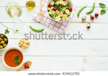 Light summer dinner / supper concept. Green salad with pasta, cherry tomato, quail eggs, olive oil. Cold tomato soup (gazpacho), croutons, green olives and glass of cold white wine.