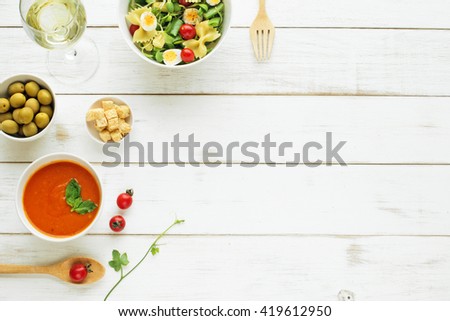 Light summer dinner / supper concept. Green salad with pasta, cherry tomato, quail eggs. Cold tomato soup (gazpacho), green olives and glass of cold white wine.