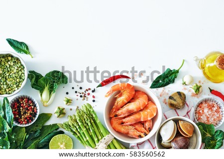 Top view of light dinner ingredients over white background with a copy space. Cooked prawns, clamps, asparagus, spinach, baby eggplant, brown rice, salt and pepper.