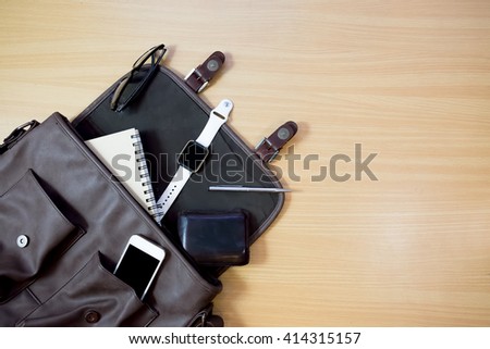 Outfit of traveler, student, teenager, young man.  Different objects on wooden background: leather bag, smart watch,smartphone, glasses, notebook and pen top view . retro style ,vintage tone