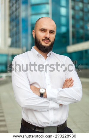 Businessman with beard in white shirt standing near office building