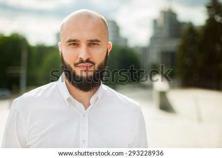 Businessman with beard in white shirt standing and looking in camera