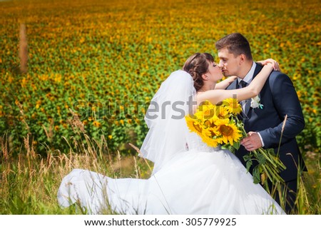 Wedding couple in the summer field with sunflowers bouquet