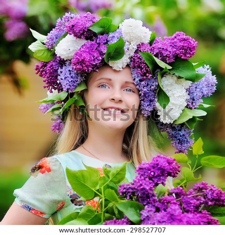Portrait of a little girl with a bouquet of flowers in her hands and a wreath of flowers of lilac color . The girl is smiling and looking at the sky. The photo was taken outdoors.