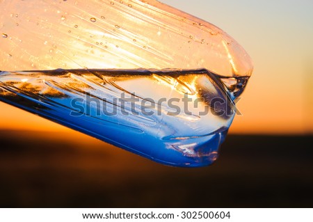 Plastic bottle with water against the sunset sun. Beams of the sun make the way through water.