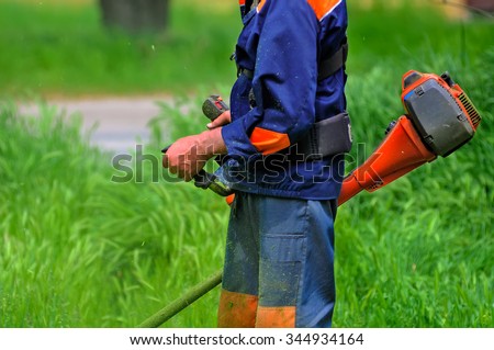 The worker of a garden cuts off a grass. The man in a uniform of the general worker works at a lawn. Work of municipal services on improvement of territories.