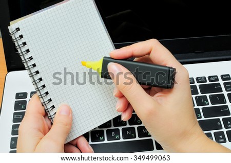 Hands with a marker and a notebook against the laptop. The person makes entries in a notebook.