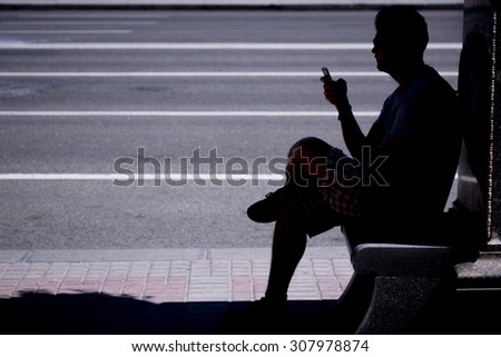Man wearing sunglasses sitting by the road texting on his phone, silhouette