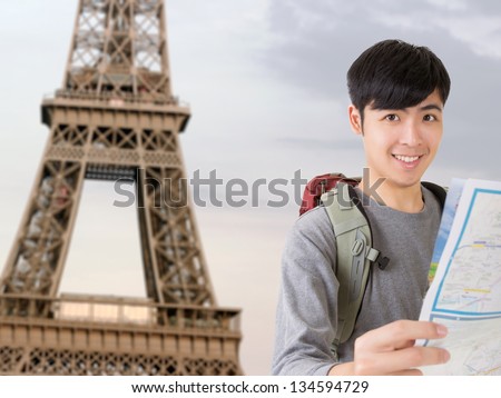 Asian young traveler of man hold map and look at you in front of the famous landmark, Eiffel Tower, France.