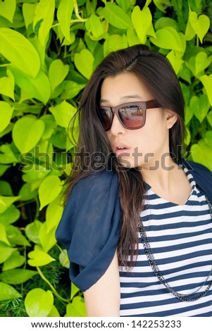 Asian attractive young woman against green plant wall, closeup portrait.