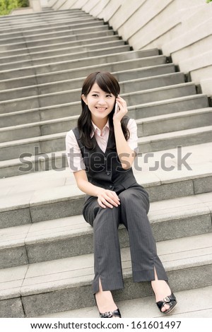 Asian business woman sit on stair and talk on cellphone in daytime urban.