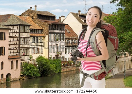 Smiling traveling Asian girl holding a camera and looking at you in the street of Europe.