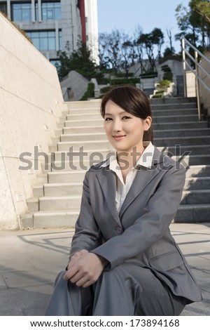 Smiling Asian business woman sit on stair of outside in modern city.