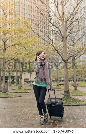 Attractive Asian woman holding suitcase and talking on phone at street, Taipei, Taiwan.