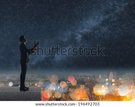 Silhouette of Asian businessman standing and praying at the roof under stars night in city.