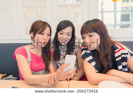 Asian lady in the restaurant and share something in mobile phone with her friends.