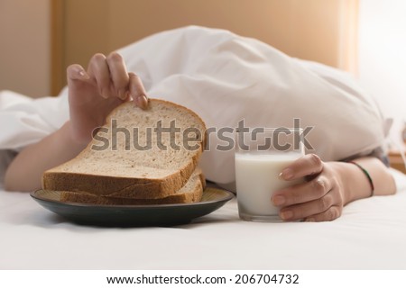 Woman\'s hand reaching from under duvet for breakfast in hotel.
