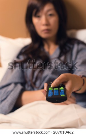 Asian woman hold the remote and watch tv on the bed.