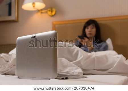 Asian woman put her laptop on bed and watch tv in the hotel.