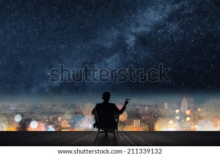 Silhouette of businessman sit on chair and hold a cigar unger the stars.
