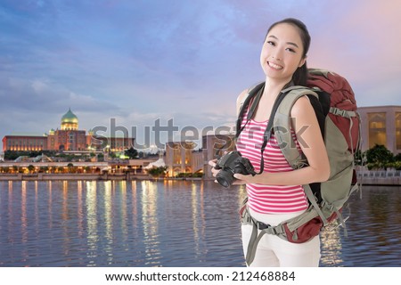 Happy smiling Asian young female backpacker with camera in Putrajaya, Malaysia.