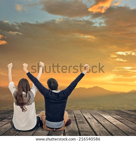 Asian couple sit on wooden ground and feel exciting against the dramatic sky with copyspace.