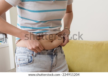 A woman is grabbing a love handles around her waist.