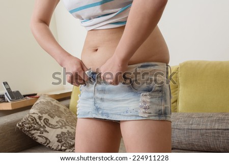 Woman trying to fasten her denim skirt.