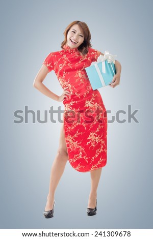 Smiling Chinese woman dress traditional cheongsam standing and holding a gift box at New Year, full length portrait  isolated.