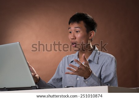 Surprised Chinese business man sitting on chair and looking at laptop in studio.