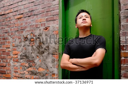 There is an Asian man stand against a old door and lonely.