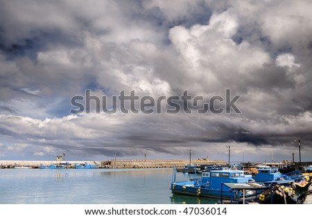 Boats on harbor under dramatic sky with storm clouds.