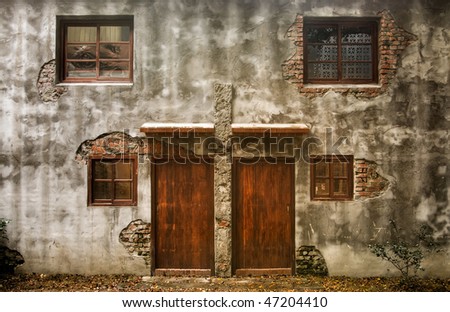 Ruins of old wall and brown door and dark windows of discarded building.