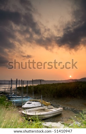 Discard boats on dried river with dramatic sky of sunset.
