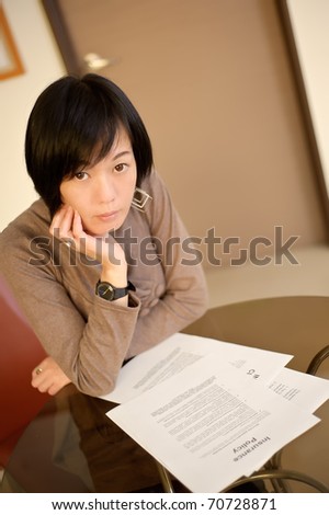 Asian woman reading insurance policy paper on desk in office.