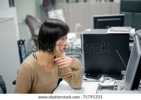 Single mature Asian woman working in office and looking at computer screen.