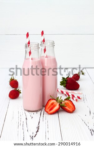Strawberry milk in traditional glass bottles with straws on old vintage wooden background