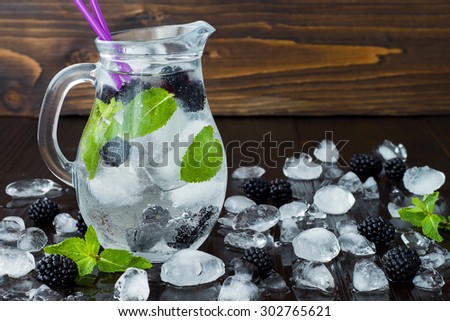 Healthy detox flavored water with blackberry and mint. Cold refreshing berry drink with ice on dark wooden table. Copy space background. Clean eating
