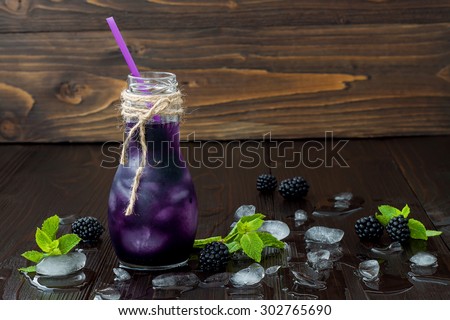 Refreshing blackberry juice in vintage eco style bottle on rustic dark wooden table. Cold summer berry drink with ice and mint. Copy space background. Clean eating