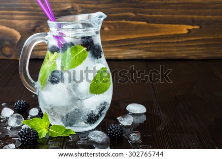 Healthy detox flavored water with blackberry and mint. Cold refreshing berry drink with ice on dark wooden table. Copy space background. Clean eating