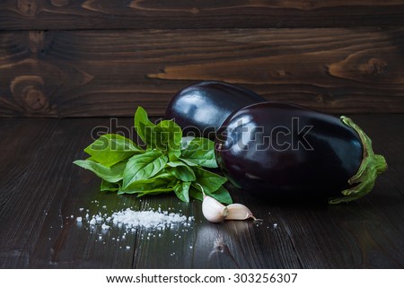 Eggplant (aubergine) with basil and garlic on dark wooden table. Fresh raw farm vegetables - harvest from the garden in rustic kitchen. Rural still life